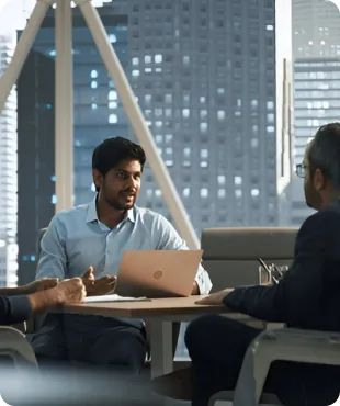 Two men and a woman engaged in a professional discussion inside a modern office with large windows showing a cityscape view.