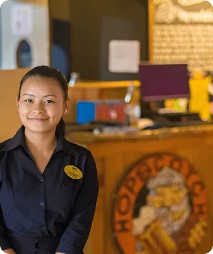 A female staff member wearing a navy-blue uniform, smiling in front of a well-lit reception desk with a colorful interior.