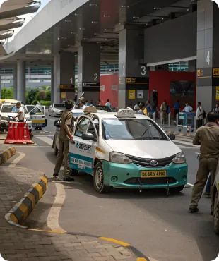 A busy outdoor airport drop-off area with taxis and travelers loading luggage.