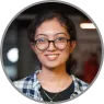 Portrait of a smiling woman wearing glasses and a casual plaid shirt, captured in a well-lit indoor setting.